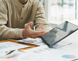 Primer plano de una persona, probablemente un asesor o cliente, señalando datos financieros en una tablet sobre un escritorio lleno de gráficos y documentos, representando una reunión de análisis y asesoría fiscal