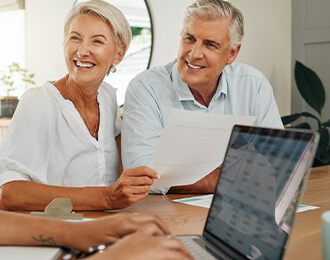Pareja de adultos mayores, sonrientes y felices, revisando documentos mientras una persona (cuyas manos se ven tecleando en un portátil) les brinda asesoría fiscal, simbolizando tranquilidad en la planificación financiera.